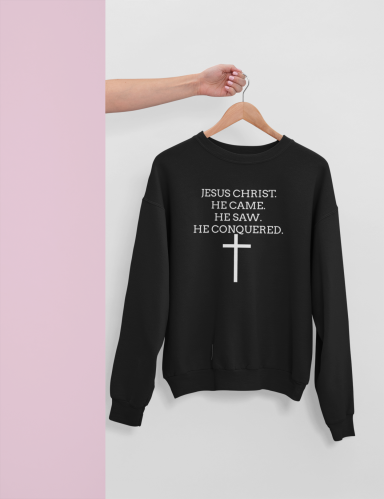 Black sweatshirt with text and a cross design, hanging on a hook against a light background.